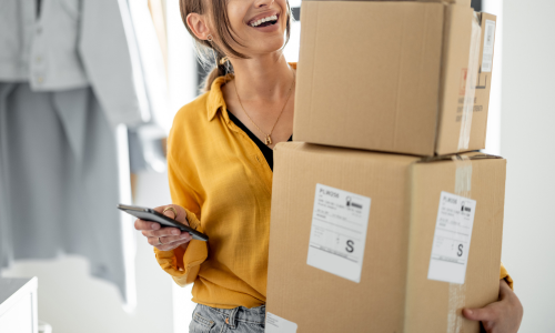 Woman smiling carrying a stack of cardboard boxes